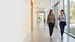 © Maksym - Two businesswomen walking and talking in modern office hallway with natural light