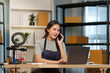 © Natee Meepian - Asian small business owner talking on smartphone and using laptop for e-commerce order management