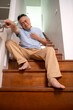 © Wosunan - Senior man sitting on a staircase and holding his chest with an expression of pain,