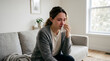 © hadi - Sad young woman sitting on sofa crying and wiping tears with tissue