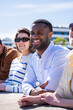 © CarlosBarquero - Vertical. Close lifestyle portrait of a cheerful Black man with friends in a bright residential area, showing friendship, diversity and relaxed outdoor leisure.