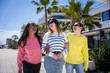 © CarlosBarquero - Multicultural female friends walk side by side and smile in a sunny residential district, sharing a casual friendship and lifestyle moment.