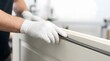 © Vatrick - Close up of worker hands in white protective gloves fitting black rubber weatherstrip seal gasket into door frame groove for soundproofing and insulation.