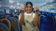 © Krakenimages.com - Woman in apron smiling, pinched fingers beckoning gesture with both hands inside airplane cabin at airport; friendly invitation.