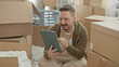 © Krakenimages.com - Man holding tablet and pointing at screen while seated among cardboard boxes in a building; moving day calm.