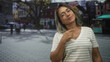 © Krakenimages.com - Woman with glasses wearing striped shirt points to her chest with her right hand on a bustling street lined with shops and trees while looking upward; quiet pride.