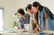 © whyframeshot - Team leaning over desk discussing strategy chart together, one colleague laughing while others focus intently, casual collaborative brainstorming session concept