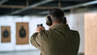 © A2Z AI  - A mature man in protective gear holding a handgun and aim at paper targets inside a modern indoor shooting range facility for practice session