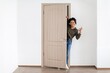 © Prostock-studio - Smiling Black Woman Showing Joyful Emotion While Peeking Through Doorway In Modern Room, Engaging With Camera And Inviting In Natural Light, Creating A Welcoming Atmosphere. Concept Of Happiness.