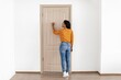 © Prostock-studio - Focused Black Female Knocking On Door With Hand, Standing In Bright Room At Home. She Exhibits Curiosity While Engaged In This Simple Home Interaction. Home And Lifestyle Concept.