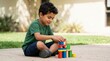 © Xenia - Smiling Arab boy playing with colorful building blocks outdoors. Young child building a tower on pavement. Early childhood education concept
