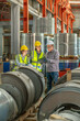 © BESTIMAGE - Engineers team inspecting metal sheet machine system inspection check collaboration in factory Female worker measuring steel coil with tape measure alongside supervisor writing notes on clipboard