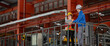 © BESTIMAGE - Engineers team discussing metal sheet machine system operation collaboration in factory Industrial male and female engineers leaning metal railing with laptop on elevated factory catwalk