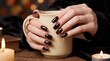 © Ammar.stock - Dark gothic manicure with black nails holding a coffee mug, cozy autumn aesthetic with candles and books, elegant hand care