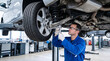 © Mirivox - Male mechanic in blue uniform and glasses working on car undercarriage on lift, representative of automotive service and repair