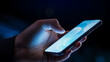 © Vyatcheslav - Close up of hand holding and touching smartphone screen in the dark. Person using mobile phone with glowing blue display. Digital technology and communication concept