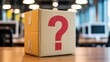 © MSTMAYA - Brown cardboard box featuring a bold red question mark symbol placed on a clean wooden desk inside a blurred modern office workspace interior