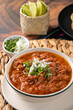 © AndreaGabriela - Mexican birria stew bowl with lime wedges and cilantro garnish, traditional comfort food