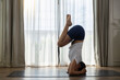 © Ratirat - woman practicing yoga headstand pose on mat by window in bright indoor room feeling peaceful and calm during morning workout