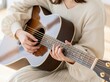 © AI-HAL8 - 温かいニットを着てアコースティックギターのコードを押さえる女性
