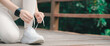 © sorapop - Female runner showing sharpened determination during sport fitness exercise preparation, athlete ties white sneaker shoelaces on wooden bridge outdoors before running workout