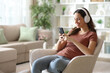 © PheelingsMedia - Happy woman on armchair listening music from phone