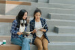 © MrAshi - Two Asian female college students using laptop with headphones while studying together on campus stairs.