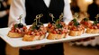 © Lubov - Waiter holds white platter with gourmet bruschetta appetizers. Italian crostini topped with tomato, onion, herbs, and olive. Ideal for events, weddings, parties, catering.