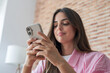 © Daniel - Young woman smiling and engaging with her mobile phone, using social media or sending text messages, highlighting concepts of communication, technology, and modern digital connection indoors