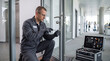 © RedCat - A man in a grey uniform is working on a glass office door lock with a screwdriver, next to a toolbox. Door repair service, professional maintenance, professional locksmith, office technician.