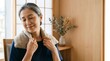 © SITI - Mature Asian woman resting on chair with heating pad wrapped around neck at home