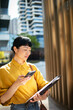 © Davor - Businesswoman using smartphone with folder on modern city street