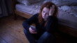 © Hifzhan Graphics - Young woman crying while holding smartphone on bedroom floor