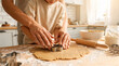 © Suraya - Hands shaping cookie dough with cutters on kitchen counter.