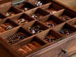© S-DESIGN - A close-up view of a wooden jewelry box filled with assorted rings, bracelets, and necklaces. The compartments are lined with soft velvet, showcasing the intricate details of each piece.