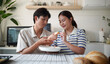 © matinee - Happy Asian couple tasting and sharing homemade cookies in the kitchen.