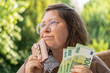 © kittyfly - Mature european woman, 50 years old presenting euro banknotes money in her hand, emotional female portrait, financial freedom, cash payments, savings, exchange and cashing currency, real people