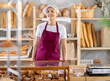 © JackF - Asian woman seller in uniform standing behind counter in bakery. Saleswoman smiles welcome and waits for customers in the baking section of the supermarket