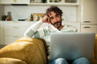 © Davor - Man using laptop on sofa in home kitchen