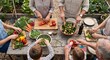 © Ash - Extended family gathers around a rustic wooden garden table outdoors to chop fresh organic vegetables and prepare a healthy communal salad together in the.