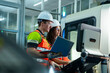 © VStudio - Team of male and female industrial engineers in safety gear using a laptop to program and control a CNC machine on a modern manufacturing factory floor. Teamwork and smart industry concept.