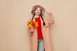 © Oleg Gekman - A beautiful young woman in an autumn fashionable outfit with shopping bags and round hat pointing aside at free space over beige background