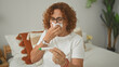 © Krakenimages.com - Middle aged hispanic woman wearing glasses holding a thermometer, wipes nose with tissue while seated on bed in bedroom; illness concern.