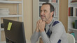 © Krakenimages.com - Man with hands clasped under chin looking at computer monitor in a building office with bookshelves and sticky note on screen; thoughtful reflection.