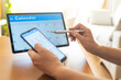© Nanci - Person organizing a busy appointment schedule on a tablet with a stylus while checking a smartphone, demonstrating efficient digital time management and modern planning skills