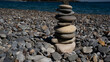 © Azur - A serene stack of smooth stones balanced atop one another on a pebbly beach, with the calming ocean in the background.