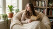 © Alex Pios - Young woman with long brown hair relaxing in a cozy armchair with a book, looking out a window in a sunlit room with plants and a bookshelf, concept of comfort and relaxation