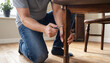 © MdNiloy - Man kneeling on wooden floor assembling and repairing a wooden table leg using a screwdriver with furniture assembly home improvement living room screwdriver handyman carpentry woodwork