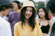 © lashkhidzetim - Young woman smiles warmly at a festival crowd. Her yellow hat and shirt add cheerful brightness. Friends surround her, engaged in casual conversation. Sunlight highlights her joyful