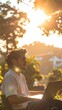 © Togar - A young man works on his laptop outdoors in the warm glow of the sun.